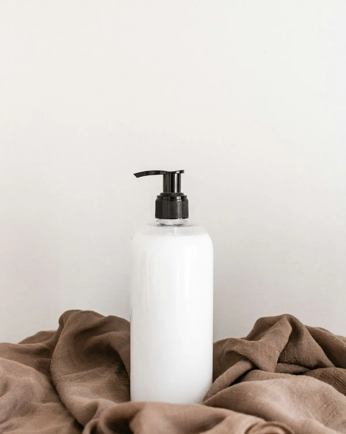 Flacon cosmétique blanc posé sur un lin naturel